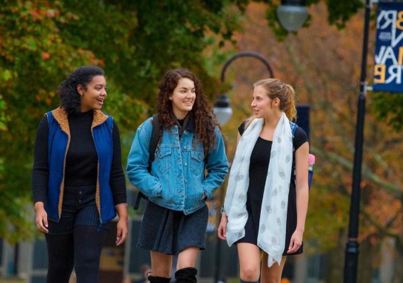 Three students walking on campus with a Bryn Mawr College flag in the background